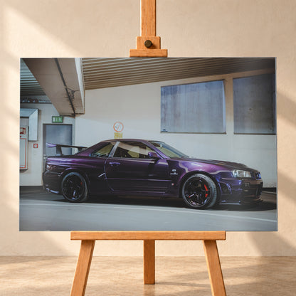 Violetter Nissan Skyline R34, nahezu seitlich mit der Front nach rechts, in einem hellen Parkgaragen-Innenraum; sichtbar sind schwarze Räder, rote Bremssättel und ein großer Heckflügel; Visualisierung als Alu gebürstet-Wandbild, frontal auf einer Holzstaffelei.