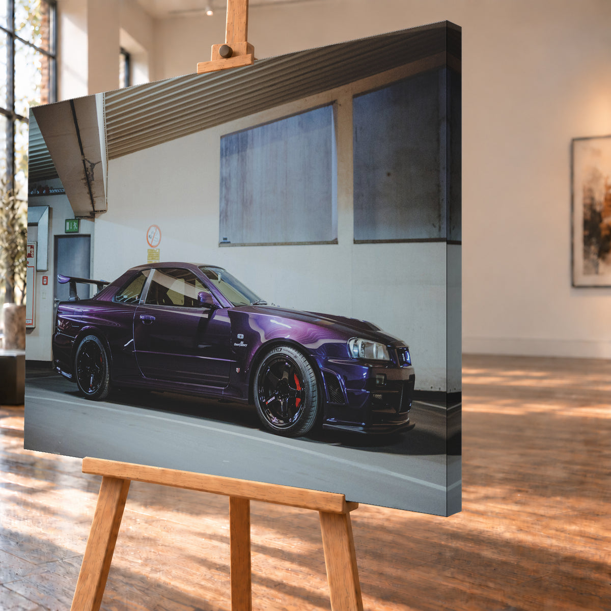 Violetter Nissan Skyline R34, nahezu seitlich mit der Front nach rechts, in einem hellen Parkgaragen-Innenraum; sichtbar sind schwarze Räder, rote Bremssättel und ein großer Heckflügel; Visualisierung als Leinwand-Wandbild, schräg von der Seite auf einer Holzstaffelei.