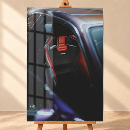 Nahaufnahme durch die geöffnete Tür eines violetten Nissan Skyline R34: Ein rot-schwarzer Sitz mit sichtbarem Nismo-Schriftzug steht im dunklen Innenraum; helle und blau-violette Reflexe verlaufen über Dachkante und Türrahmen; Visualisierung als Acrylglas-Wandbild, frontal auf einer Holzstaffelei.