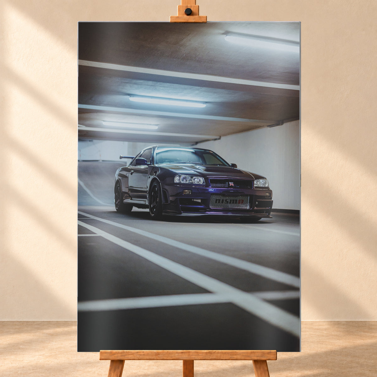 Dunkelvioletter Nissan Skyline R34 in niedriger Frontdreiviertelansicht in einer Beton-Parkgarage. Weiße Fahrbahnmarkierungen führen zum Fahrzeug; kühle Deckenleuchten spiegeln sich auf Haube und Scheibe. Sichtbar sind dunkle Räder und ein großer Heckflügel; Visualisierung als Alu gebürstet-Wandbild, frontal auf einer Holzstaffelei.