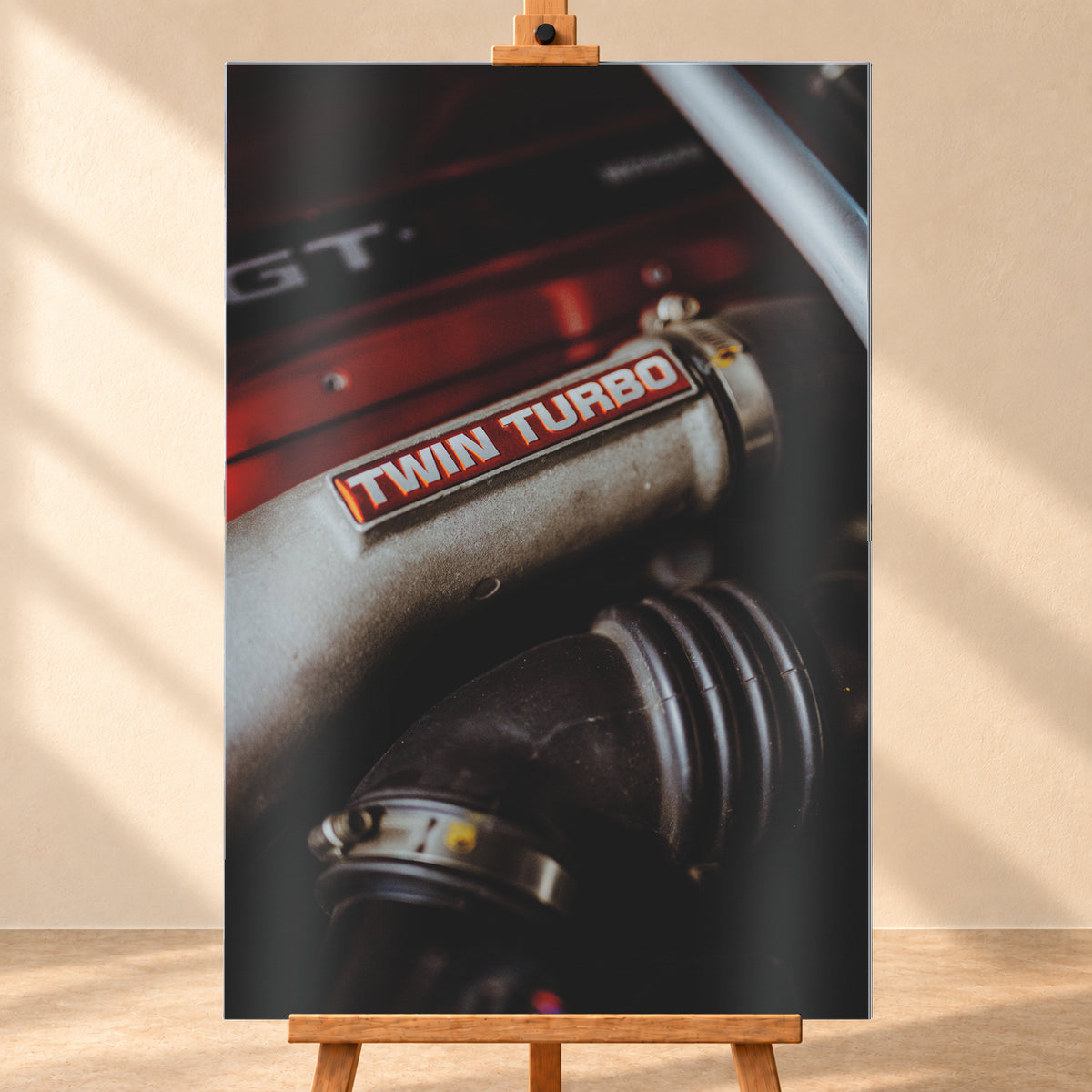 Detailaufnahme eines Motorraums mit metallisch grauem Bauteil und rot-weißem „TWIN TURBO“-Schriftzug. Schwarze gerippte Schläuche, rote Flächen, ein helles diagonales Element und geringe Schärfentiefe prägen das dunkle Bild; Visualisierung als Alu gebürstet-Wandbild, frontal auf einer Holzstaffelei.