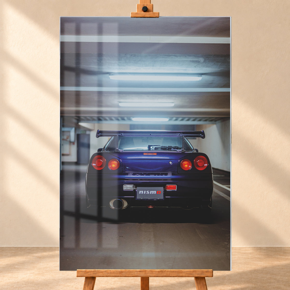 Mittige Heckansicht eines dunkelvioletten Nissan Skyline R34 in einer Parkgarage. Vier runde rote Rückleuchten, davon die beiden inneren orange leuchtend, ein großer Heckflügel, ein rundes Auspuffendrohr und ein Nismo-Schriftzug sind unter kühlen, horizontalen Deckenleuchten zu sehen; Visualisierung als Acrylglas-Wandbild, frontal auf einer Holzstaffelei.