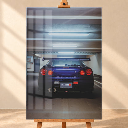 Mittige Heckansicht eines dunkelvioletten Nissan Skyline R34 in einer Parkgarage. Vier runde rote Rückleuchten, davon die beiden inneren orange leuchtend, ein großer Heckflügel, ein rundes Auspuffendrohr und ein Nismo-Schriftzug sind unter kühlen, horizontalen Deckenleuchten zu sehen; Visualisierung als Acrylglas-Wandbild, frontal auf einer Holzstaffelei.
