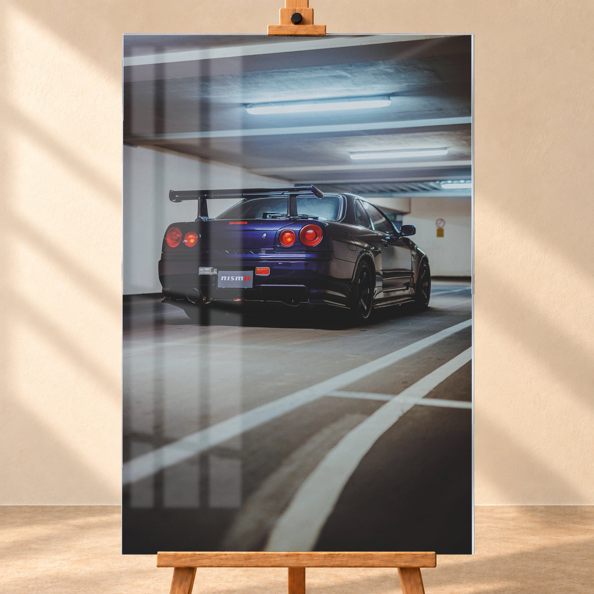 Dunkelvioletter Nissan Skyline R34 in tiefer Heck-Dreiviertelansicht in einer Beton-Parkgarage. Sichtbar sind vier rote Rundlichter, ein großer Heckflügel, dunkle Räder, ein großes Auspuffendrohr, weiße Fahrbahnlinien und kühle Deckenleuchten; Visualisierung als Acrylglas-Wandbild, frontal auf einer Holzstaffelei.