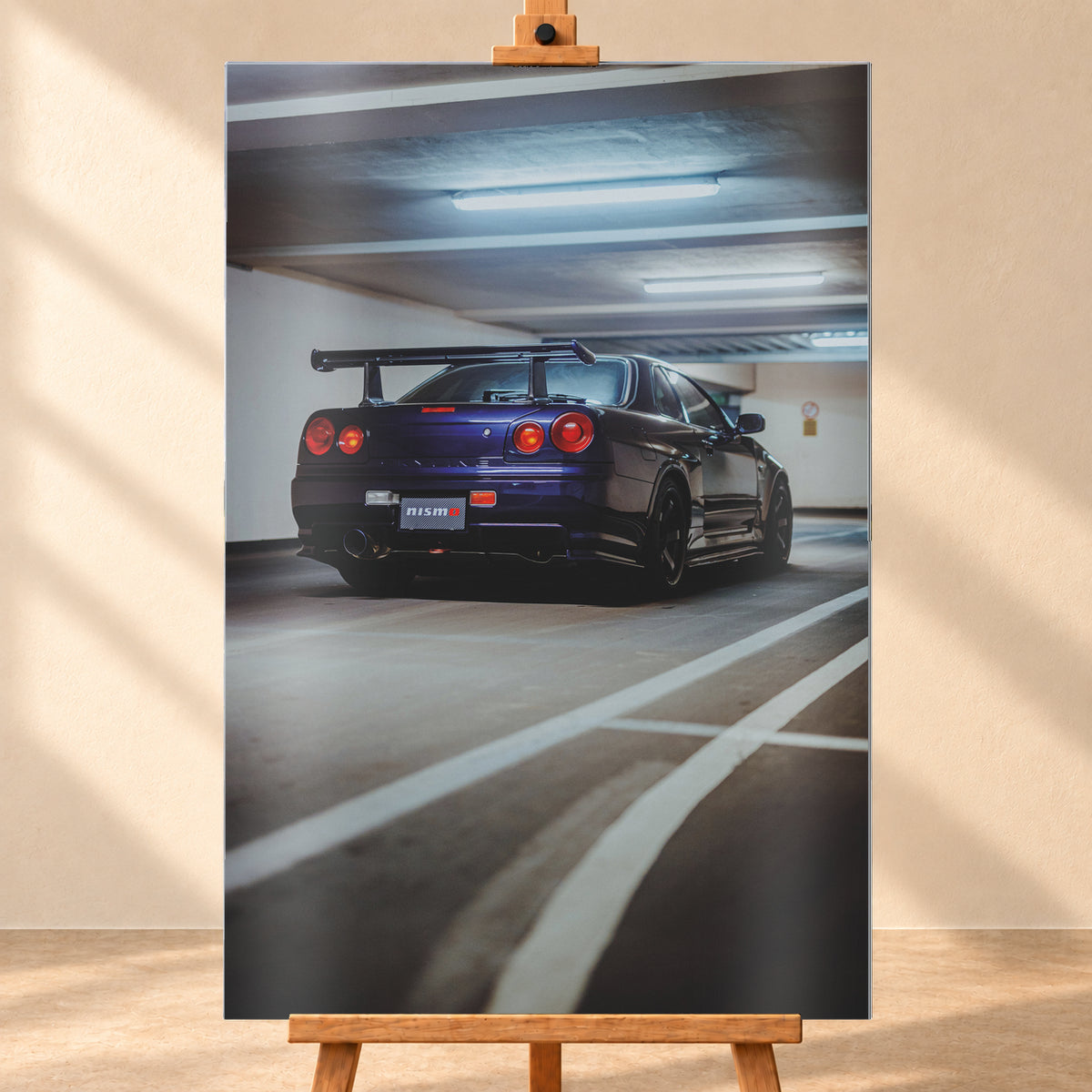 Dunkelvioletter Nissan Skyline R34 in tiefer Heck-Dreiviertelansicht in einer Beton-Parkgarage. Sichtbar sind vier rote Rundlichter, ein großer Heckflügel, dunkle Räder, ein großes Auspuffendrohr, weiße Fahrbahnlinien und kühle Deckenleuchten; Visualisierung als Alu gebürstet-Wandbild, frontal auf einer Holzstaffelei.