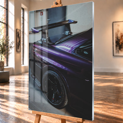 Nahaufnahme der hinteren Seitenpartie eines violetten Nissan Skyline R34 in einem Innenraum; sichtbar sind schwarzes Hinterrad, Radlauf, Heckscheibe und großer Heckflügel mit hellen Reflexionen; Visualisierung als Acrylglas-Wandbild, schräg von der Seite auf einer Holzstaffelei.