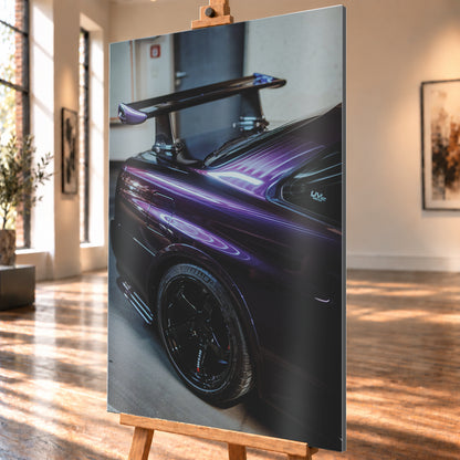 Nahaufnahme der hinteren Seitenpartie eines violetten Nissan Skyline R34 in einem Innenraum; sichtbar sind schwarzes Hinterrad, Radlauf, Heckscheibe und großer Heckflügel mit hellen Reflexionen; Visualisierung als Alu gebürstet-Wandbild, schräg von der Seite auf einer Holzstaffelei.