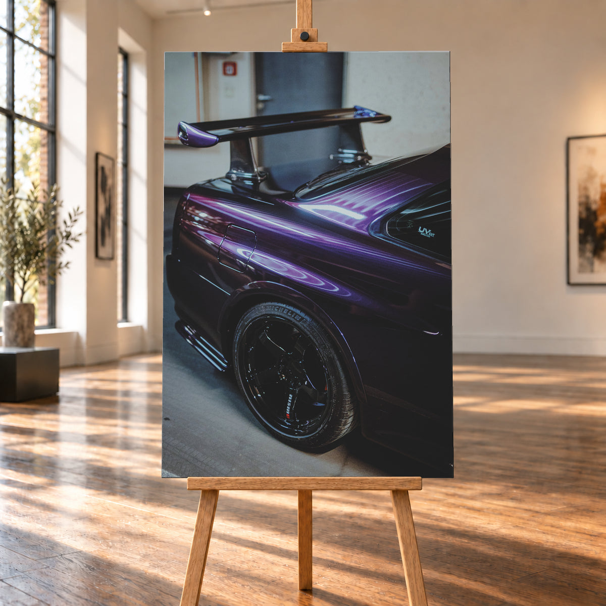 Nahaufnahme der hinteren Seitenpartie eines violetten Nissan Skyline R34 in einem Innenraum; sichtbar sind schwarzes Hinterrad, Radlauf, Heckscheibe und großer Heckflügel mit hellen Reflexionen; Visualisierung als Leinwand-Wandbild, auf einer Holzstaffelei in einem hellen Galerieraum.