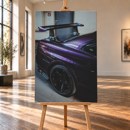 Nahaufnahme der hinteren Seitenpartie eines violetten Nissan Skyline R34 in einem Innenraum; sichtbar sind schwarzes Hinterrad, Radlauf, Heckscheibe und großer Heckflügel mit hellen Reflexionen; Visualisierung als Leinwand-Wandbild, auf einer Holzstaffelei in einem hellen Galerieraum.