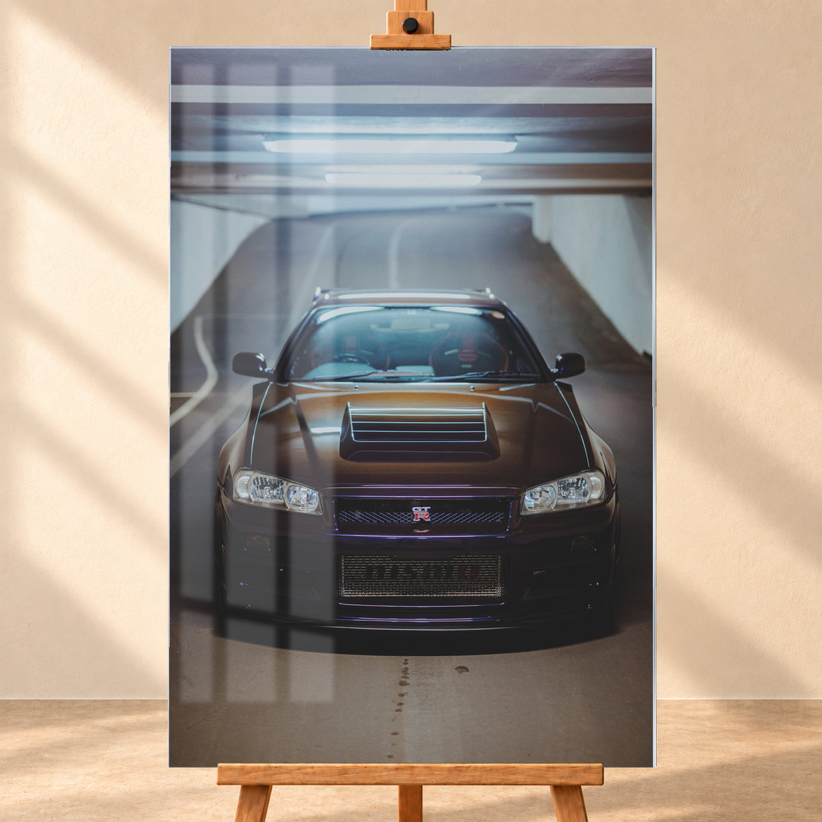 Frontale Ansicht eines dunkelvioletten Nissan Skyline R34 mit sichtbarem GT-R-Emblem in einer Tiefgarage, unter kühlen Deckenleuchten vor einer ansteigenden Fahrbahn; Visualisierung als Acrylglas-Wandbild, frontal auf einer Holzstaffelei.