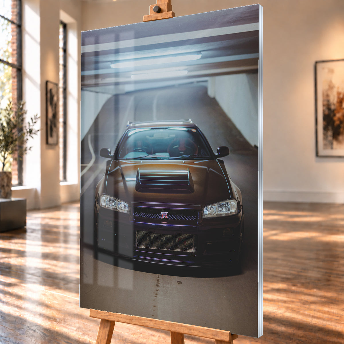 Frontale Ansicht eines dunkelvioletten Nissan Skyline R34 mit sichtbarem GT-R-Emblem in einer Tiefgarage, unter kühlen Deckenleuchten vor einer ansteigenden Fahrbahn; Visualisierung als Acrylglas-Wandbild, schräg von der Seite auf einer Holzstaffelei.