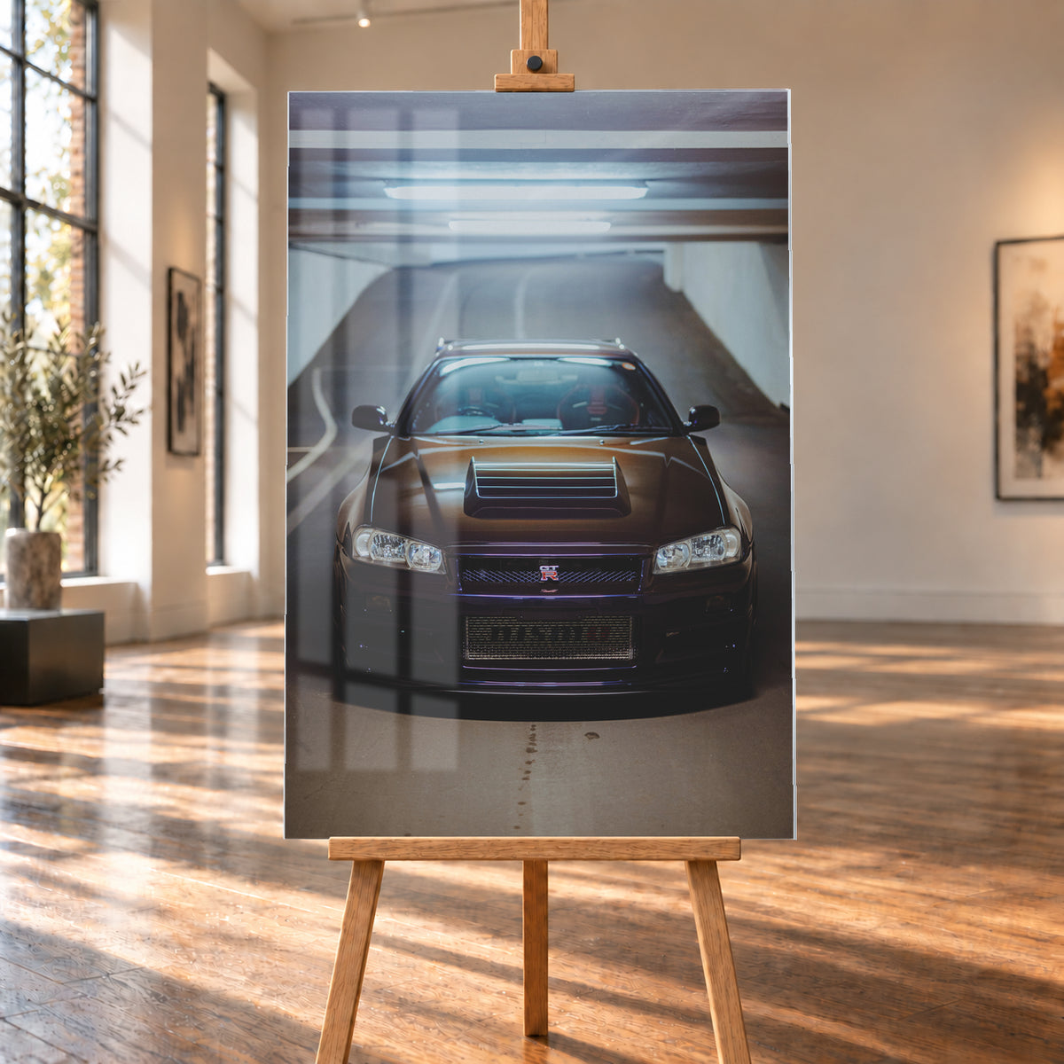 Frontale Ansicht eines dunkelvioletten Nissan Skyline R34 mit sichtbarem GT-R-Emblem in einer Tiefgarage, unter kühlen Deckenleuchten vor einer ansteigenden Fahrbahn; Visualisierung als Acrylglas-Wandbild, auf einer Holzstaffelei in einem hellen Galerieraum.