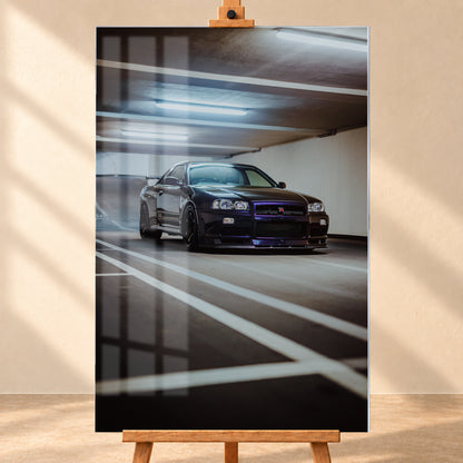 Dunkler Nissan Skyline R34 GT-R in niedriger Front-Dreiviertelansicht in einer Beton-Parkgarage, mit violett-blauen Reflexen, dunklen Rädern, Heckflügel, weißen Fahrbahnlinien und kühlen Deckenleuchten; Visualisierung als Acrylglas-Wandbild, frontal auf einer Holzstaffelei.