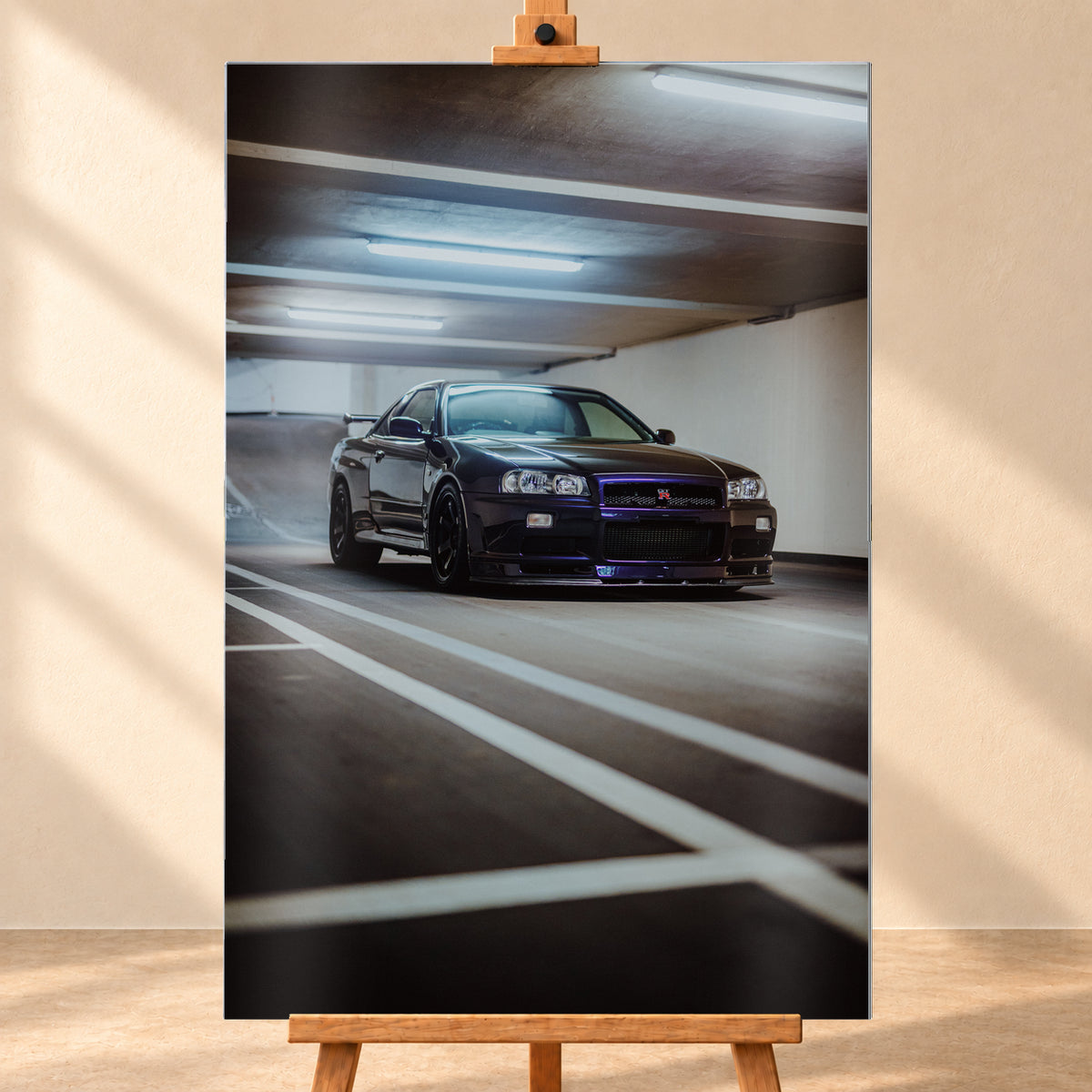 Dunkler Nissan Skyline R34 GT-R in niedriger Front-Dreiviertelansicht in einer Beton-Parkgarage, mit violett-blauen Reflexen, dunklen Rädern, Heckflügel, weißen Fahrbahnlinien und kühlen Deckenleuchten; Visualisierung als Alu gebürstet-Wandbild, frontal auf einer Holzstaffelei.