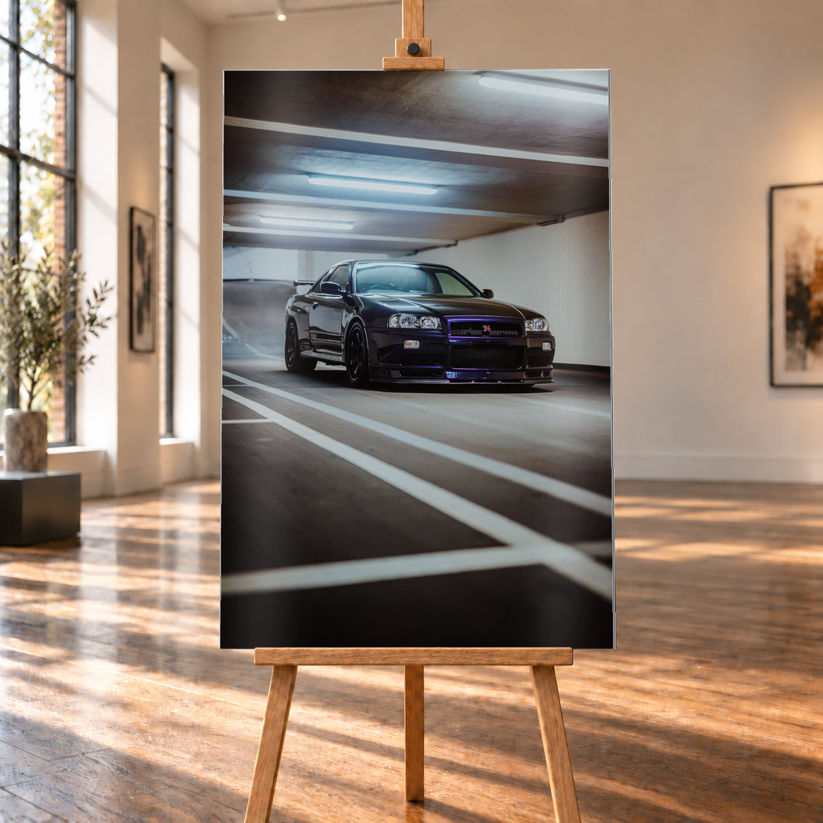 Dunkler Nissan Skyline R34 GT-R in niedriger Front-Dreiviertelansicht in einer Beton-Parkgarage, mit violett-blauen Reflexen, dunklen Rädern, Heckflügel, weißen Fahrbahnlinien und kühlen Deckenleuchten; Visualisierung als Alu gebürstet-Wandbild, auf einer Holzstaffelei in einem hellen Galerieraum.