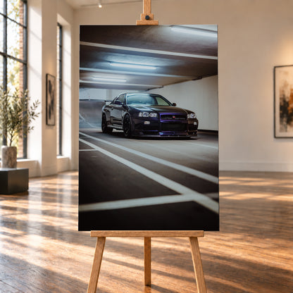 Dunkler Nissan Skyline R34 GT-R in niedriger Front-Dreiviertelansicht in einer Beton-Parkgarage, mit violett-blauen Reflexen, dunklen Rädern, Heckflügel, weißen Fahrbahnlinien und kühlen Deckenleuchten; Visualisierung als Leinwand-Wandbild, auf einer Holzstaffelei in einem hellen Galerieraum.