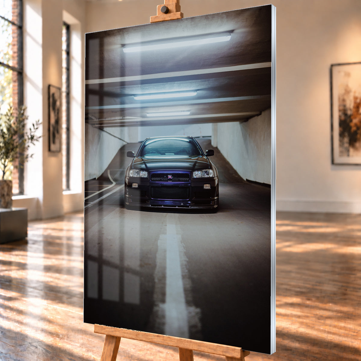 Dunkler Nissan Skyline R34 in frontaler Ansicht auf einer Betonrampe, unter kühlen weißen Deckenleuchten, mit mittiger Fahrbahnmarkierung und violettblauen Reflexen an Kühlergrill und Frontschürze; Visualisierung als Acrylglas-Wandbild, schräg von der Seite auf einer Holzstaffelei.
