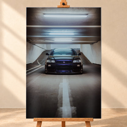 Dunkler Nissan Skyline R34 in frontaler Ansicht auf einer Betonrampe, unter kühlen weißen Deckenleuchten, mit mittiger Fahrbahnmarkierung und violettblauen Reflexen an Kühlergrill und Frontschürze; Visualisierung als Alu gebürstet-Wandbild, frontal auf einer Holzstaffelei.