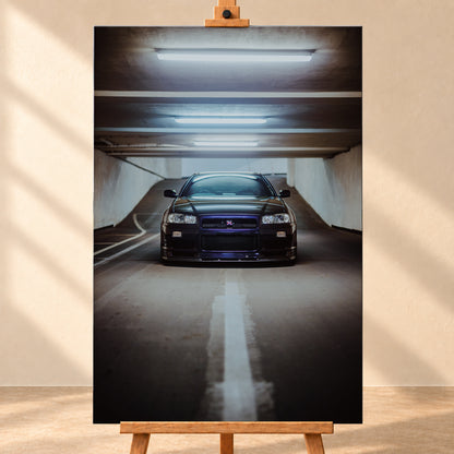 Dunkler Nissan Skyline R34 in frontaler Ansicht auf einer Betonrampe, unter kühlen weißen Deckenleuchten, mit mittiger Fahrbahnmarkierung und violettblauen Reflexen an Kühlergrill und Frontschürze; Visualisierung als Leinwand-Wandbild, frontal auf einer Holzstaffelei.