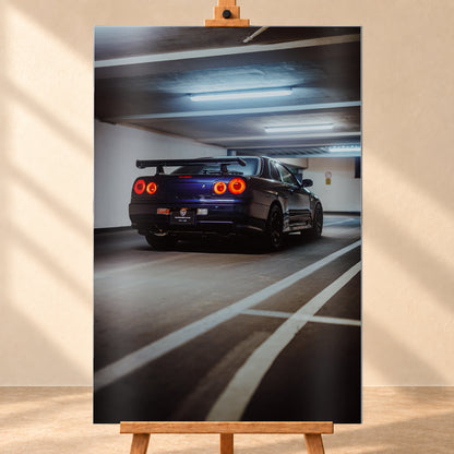 Dunkelblauer Nissan Skyline R34 in tiefer Dreiviertel-Heckansicht in einer Parkgarage; vier rote Rundrücklichter leuchten unter kühlen Deckenlampen, weiße Bodenlinien führen durch das Hochformat; Visualisierung als Alu gebürstet-Wandbild, frontal auf einer Holzstaffelei.