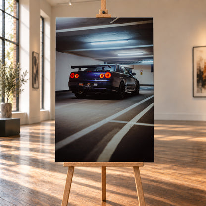 Dunkelblauer Nissan Skyline R34 in tiefer Dreiviertel-Heckansicht in einer Parkgarage; vier rote Rundrücklichter leuchten unter kühlen Deckenlampen, weiße Bodenlinien führen durch das Hochformat; Visualisierung als Leinwand-Wandbild, auf einer Holzstaffelei in einem hellen Galerieraum.