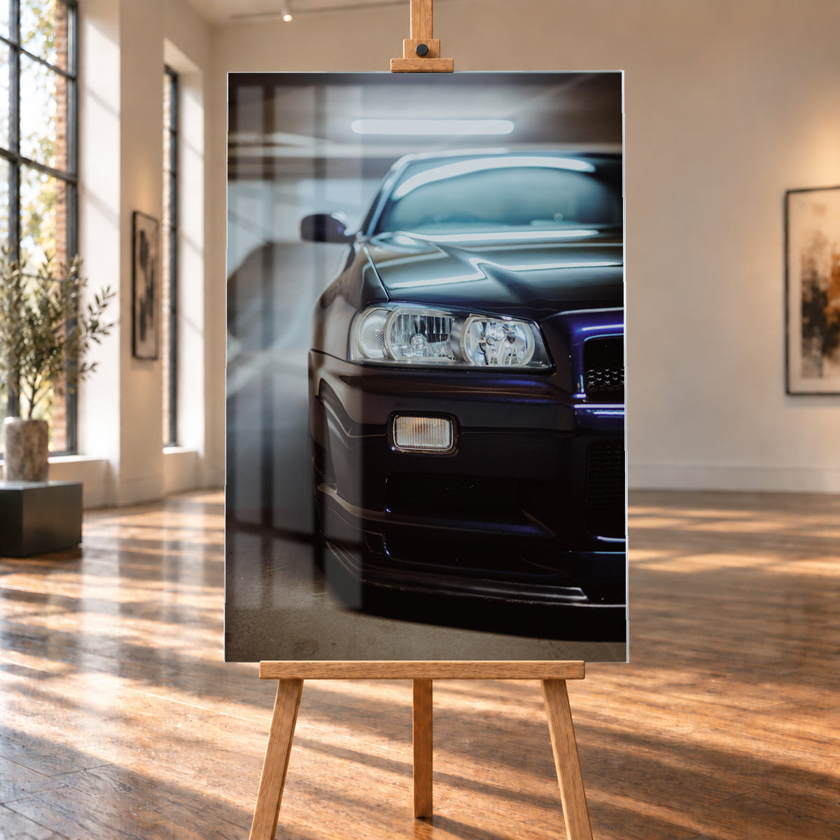 Dunkler Nissan Skyline in naher, leicht versetzter Frontansicht in einem Parkhaus. Sichtbar sind Scheinwerfer, Stoßfänger, Motorhaube, Windschutzscheibe und Seitenspiegel mit kühlen blau-violetten Lichtreflexen; Visualisierung als Acrylglas-Wandbild, auf einer Holzstaffelei in einem hellen Galerieraum.