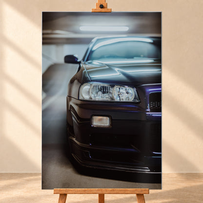 Dunkler Nissan Skyline in naher, leicht versetzter Frontansicht in einem Parkhaus. Sichtbar sind Scheinwerfer, Stoßfänger, Motorhaube, Windschutzscheibe und Seitenspiegel mit kühlen blau-violetten Lichtreflexen; Visualisierung als Alu gebürstet-Wandbild, frontal auf einer Holzstaffelei.