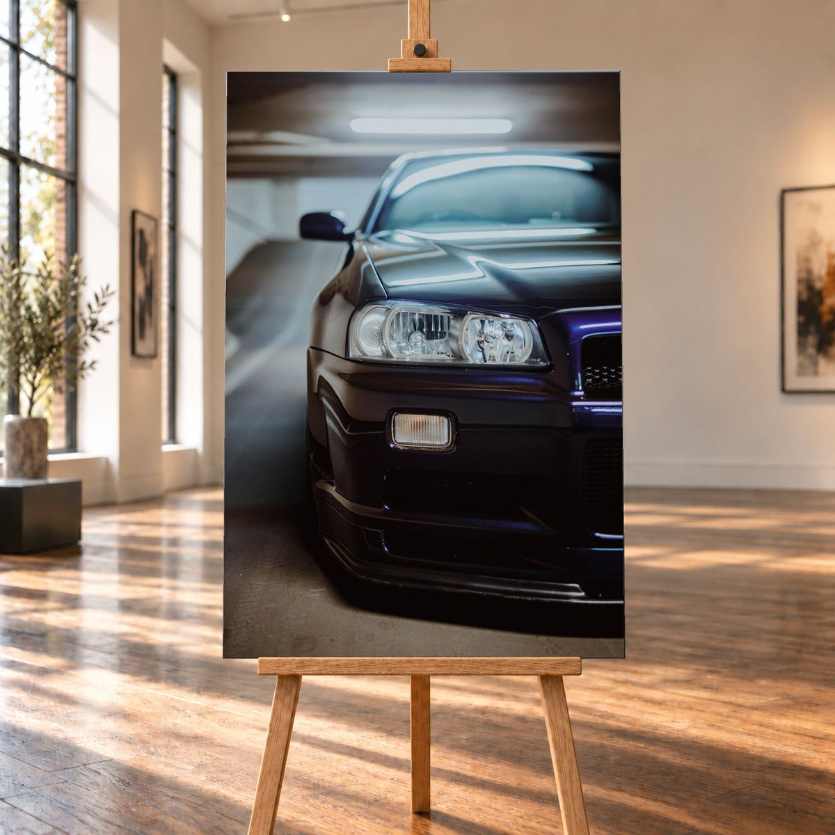 Dunkler Nissan Skyline in naher, leicht versetzter Frontansicht in einem Parkhaus. Sichtbar sind Scheinwerfer, Stoßfänger, Motorhaube, Windschutzscheibe und Seitenspiegel mit kühlen blau-violetten Lichtreflexen; Visualisierung als Leinwand-Wandbild, auf einer Holzstaffelei in einem hellen Galerieraum.