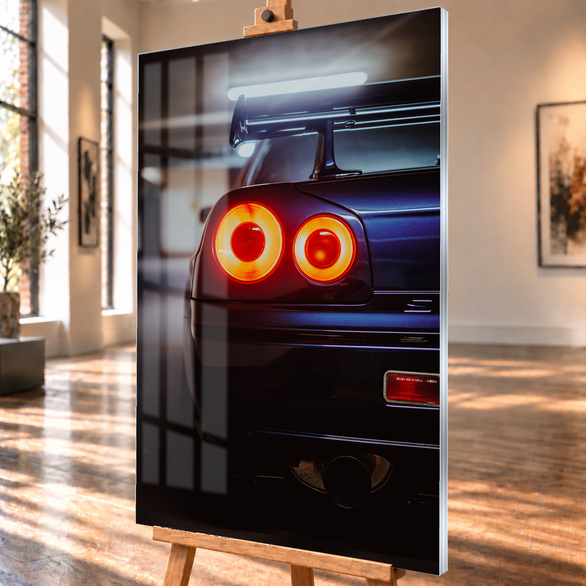 Nahaufnahme der Heckpartie eines dunklen Nissan Skyline R34 V-Spec mit zwei sichtbaren, rot-orange leuchtenden Rundrückleuchten, großem Heckflügel und rundem Auspuffendrohr vor unscharfem, kühl beleuchtetem Hintergrund; Visualisierung als Acrylglas-Wandbild, schräg von der Seite auf einer Holzstaffelei.