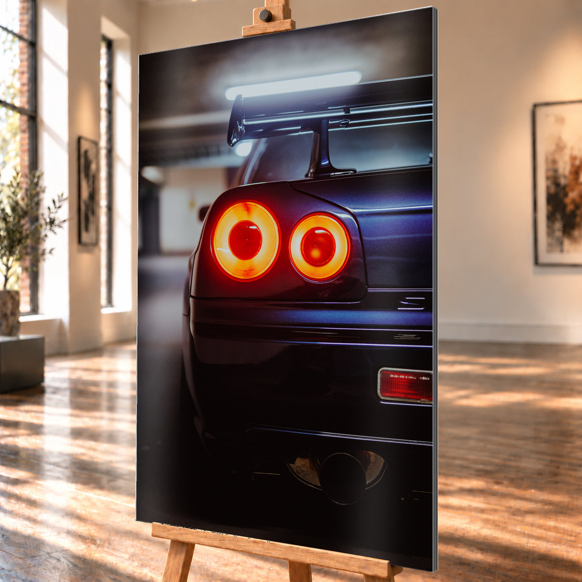 Nahaufnahme der Heckpartie eines dunklen Nissan Skyline R34 V-Spec mit zwei sichtbaren, rot-orange leuchtenden Rundrückleuchten, großem Heckflügel und rundem Auspuffendrohr vor unscharfem, kühl beleuchtetem Hintergrund; Visualisierung als Alu gebürstet-Wandbild, schräg von der Seite auf einer Holzstaffelei.