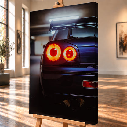 Nahaufnahme der Heckpartie eines dunklen Nissan Skyline R34 V-Spec mit zwei sichtbaren, rot-orange leuchtenden Rundrückleuchten, großem Heckflügel und rundem Auspuffendrohr vor unscharfem, kühl beleuchtetem Hintergrund; Visualisierung als Leinwand-Wandbild, schräg von der Seite auf einer Holzstaffelei.