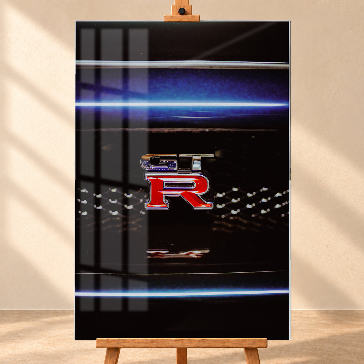 Hochformatige Nahaufnahme eines rot-silbernen GT-R-Emblems auf einem schwarzen Wabengrill. Blaue horizontale Lichtbänder verlaufen ober- und unterhalb; kleine helle Reflexe glitzern in der dunklen Fläche; Visualisierung als Acrylglas-Wandbild, frontal auf einer Holzstaffelei.