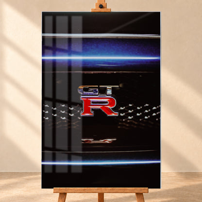 Hochformatige Nahaufnahme eines rot-silbernen GT-R-Emblems auf einem schwarzen Wabengrill. Blaue horizontale Lichtbänder verlaufen ober- und unterhalb; kleine helle Reflexe glitzern in der dunklen Fläche; Visualisierung als Acrylglas-Wandbild, frontal auf einer Holzstaffelei.