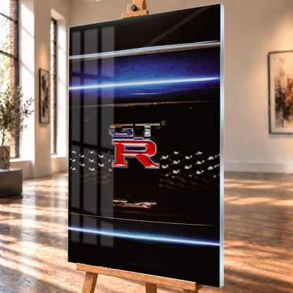 Hochformatige Nahaufnahme eines rot-silbernen GT-R-Emblems auf einem schwarzen Wabengrill. Blaue horizontale Lichtbänder verlaufen ober- und unterhalb; kleine helle Reflexe glitzern in der dunklen Fläche; Visualisierung als Acrylglas-Wandbild, schräg von der Seite auf einer Holzstaffelei.