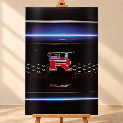 Hochformatige Nahaufnahme eines rot-silbernen GT-R-Emblems auf einem schwarzen Wabengrill. Blaue horizontale Lichtbänder verlaufen ober- und unterhalb; kleine helle Reflexe glitzern in der dunklen Fläche; Visualisierung als Alu gebürstet-Wandbild, frontal auf einer Holzstaffelei.
