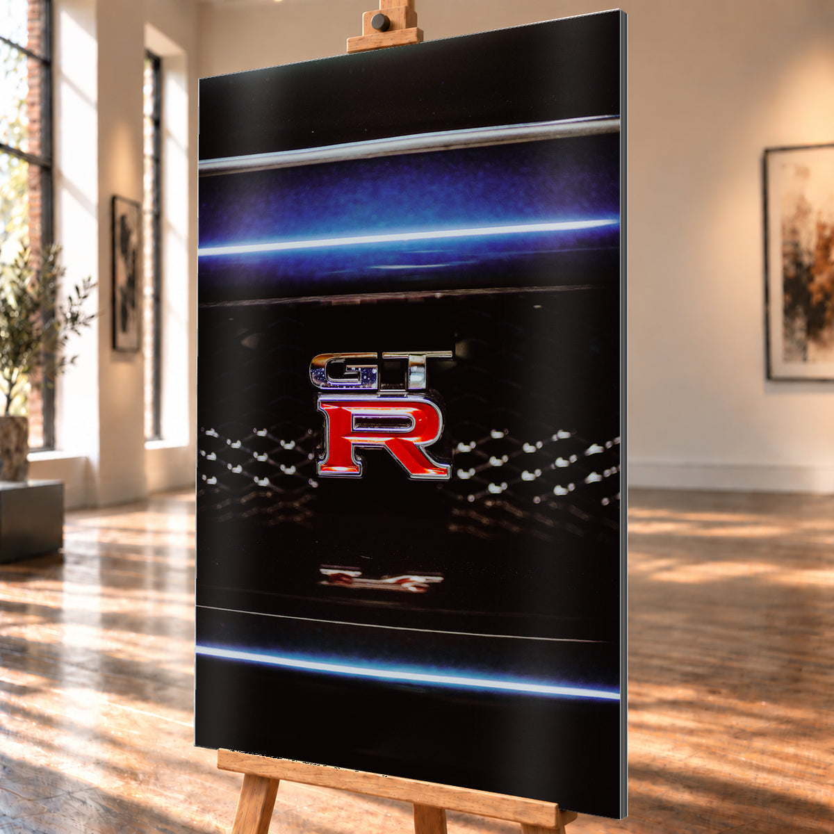 Hochformatige Nahaufnahme eines rot-silbernen GT-R-Emblems auf einem schwarzen Wabengrill. Blaue horizontale Lichtbänder verlaufen ober- und unterhalb; kleine helle Reflexe glitzern in der dunklen Fläche; Visualisierung als Alu gebürstet-Wandbild, schräg von der Seite auf einer Holzstaffelei.