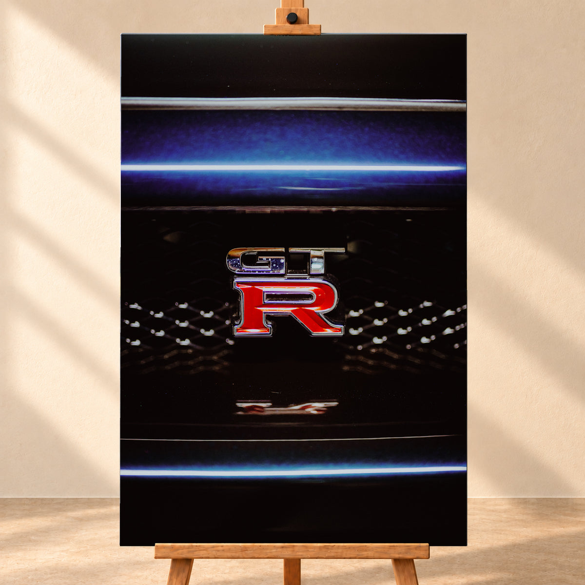 Hochformatige Nahaufnahme eines rot-silbernen GT-R-Emblems auf einem schwarzen Wabengrill. Blaue horizontale Lichtbänder verlaufen ober- und unterhalb; kleine helle Reflexe glitzern in der dunklen Fläche; Visualisierung als Leinwand-Wandbild, frontal auf einer Holzstaffelei.