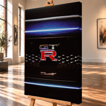 Hochformatige Nahaufnahme eines rot-silbernen GT-R-Emblems auf einem schwarzen Wabengrill. Blaue horizontale Lichtbänder verlaufen ober- und unterhalb; kleine helle Reflexe glitzern in der dunklen Fläche; Visualisierung als Leinwand-Wandbild, schräg von der Seite auf einer Holzstaffelei.