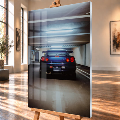 Dunkelblau bis violett wirkender Nissan Skyline R34 von hinten, mittig in einem Betonparkdeck unter kühlen Deckenleuchten; vier rote Rundlichter und ein großer Heckflügel sind sichtbar; Visualisierung als Acrylglas-Wandbild, schräg von der Seite auf einer Holzstaffelei.