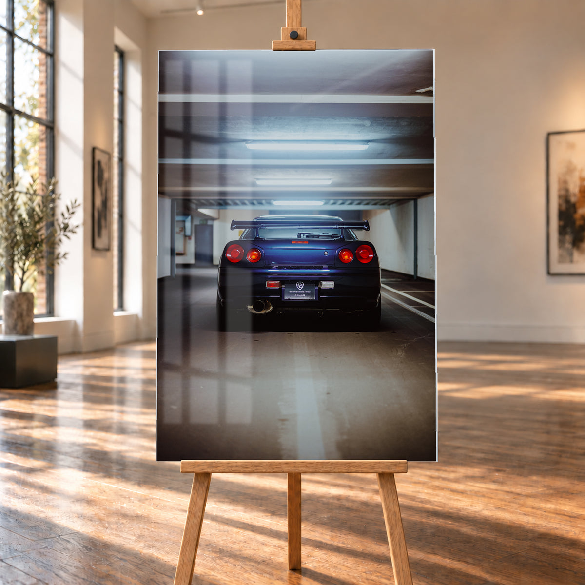 Dunkelblau bis violett wirkender Nissan Skyline R34 von hinten, mittig in einem Betonparkdeck unter kühlen Deckenleuchten; vier rote Rundlichter und ein großer Heckflügel sind sichtbar; Visualisierung als Acrylglas-Wandbild, auf einer Holzstaffelei in einem hellen Galerieraum.