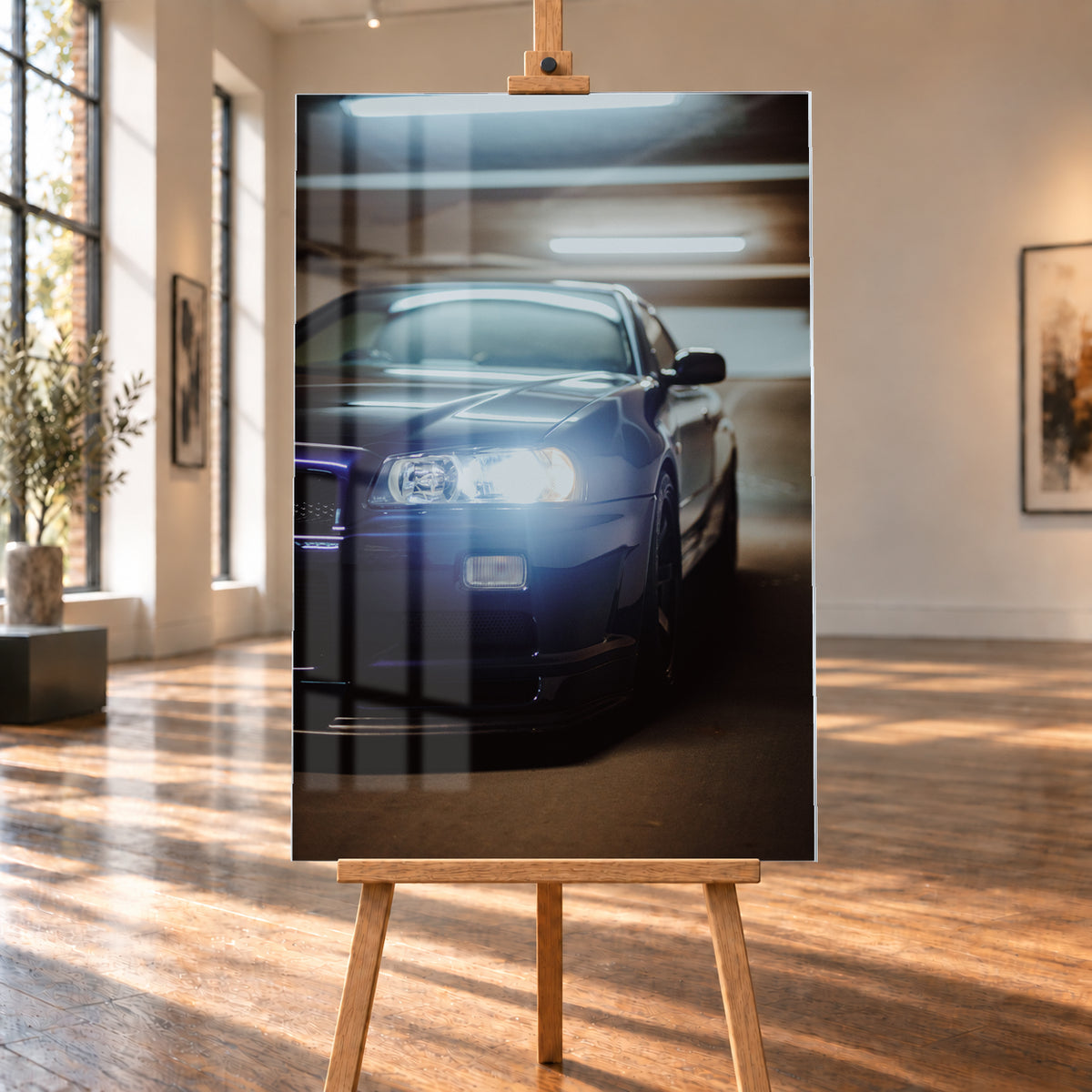 Hochformatige Nahaufnahme eines dunkelblau bis schwarz wirkenden Nissan Skyline R34 in schräger Frontansicht. Ein heller Frontscheinwerfer leuchtet in die Kamera, während sich kühle rechteckige Deckenlichter auf Motorhaube und Windschutzscheibe spiegeln. Das Fahrzeug steht in einem warm beleuchteten, unscharfen Innenraum; Visualisierung als Acrylglas-Wandbild, auf einer Holzstaffelei in einem hellen Galerieraum.