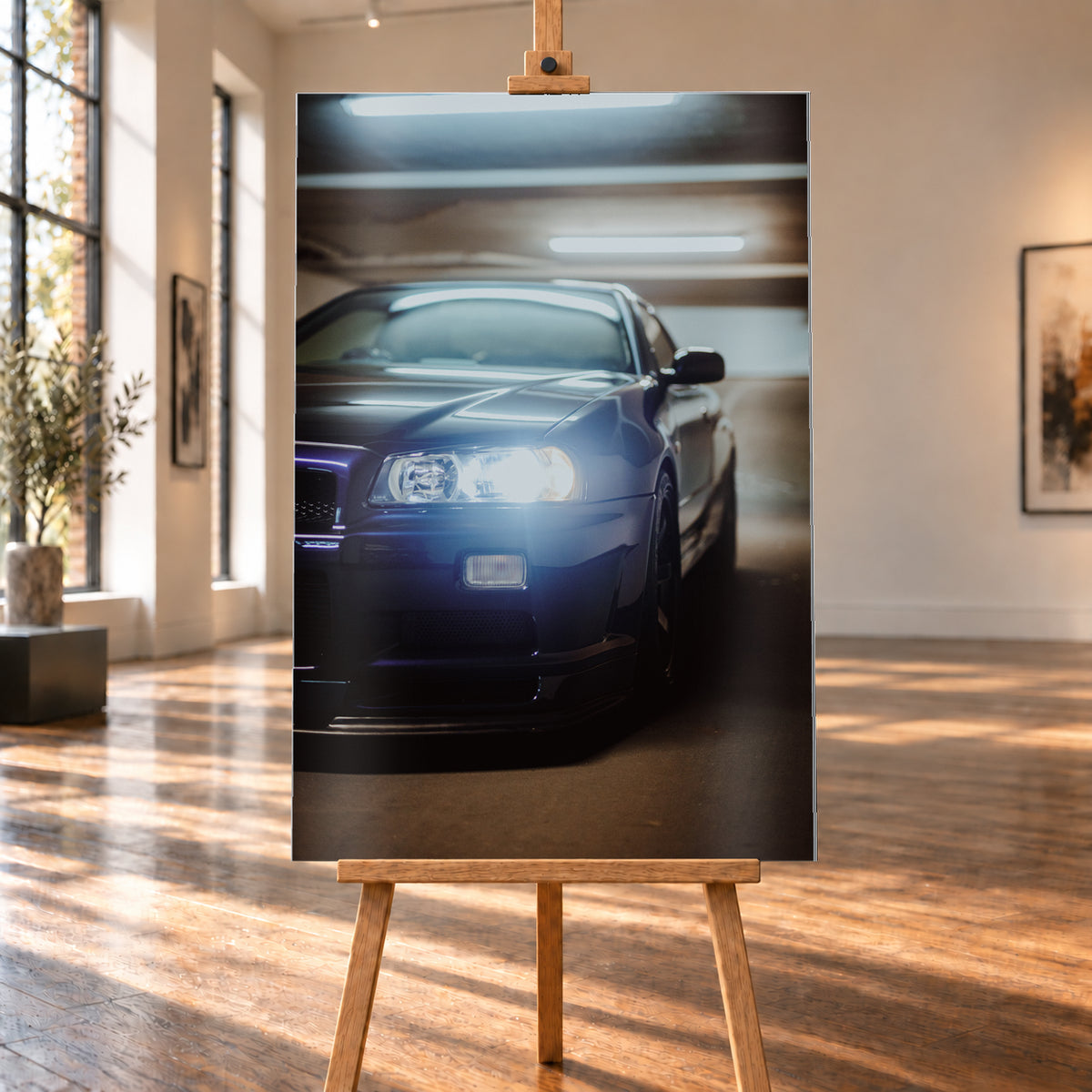 Hochformatige Nahaufnahme eines dunkelblau bis schwarz wirkenden Nissan Skyline R34 in schräger Frontansicht. Ein heller Frontscheinwerfer leuchtet in die Kamera, während sich kühle rechteckige Deckenlichter auf Motorhaube und Windschutzscheibe spiegeln. Das Fahrzeug steht in einem warm beleuchteten, unscharfen Innenraum; Visualisierung als Alu gebürstet-Wandbild, auf einer Holzstaffelei in einem hellen Galerieraum.
