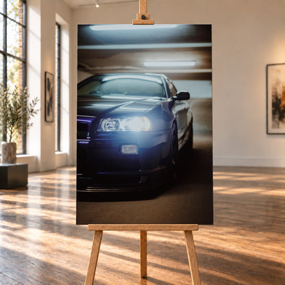 Hochformatige Nahaufnahme eines dunkelblau bis schwarz wirkenden Nissan Skyline R34 in schräger Frontansicht. Ein heller Frontscheinwerfer leuchtet in die Kamera, während sich kühle rechteckige Deckenlichter auf Motorhaube und Windschutzscheibe spiegeln. Das Fahrzeug steht in einem warm beleuchteten, unscharfen Innenraum; Visualisierung als Leinwand-Wandbild, auf einer Holzstaffelei in einem hellen Galerieraum.