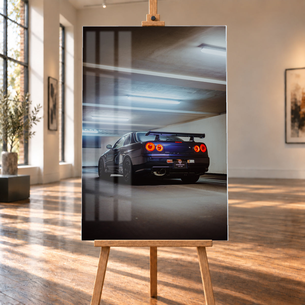 Dunkler Nissan Skyline R34 in niedriger Heck-Dreiviertelansicht mit vier rot leuchtenden Rundrückleuchten, großem Heckflügel und sichtbarem Auspuff in einer Beton-Parkgarage unter kühlen Deckenleuchten; Visualisierung als Acrylglas-Wandbild, auf einer Holzstaffelei in einem hellen Galerieraum.