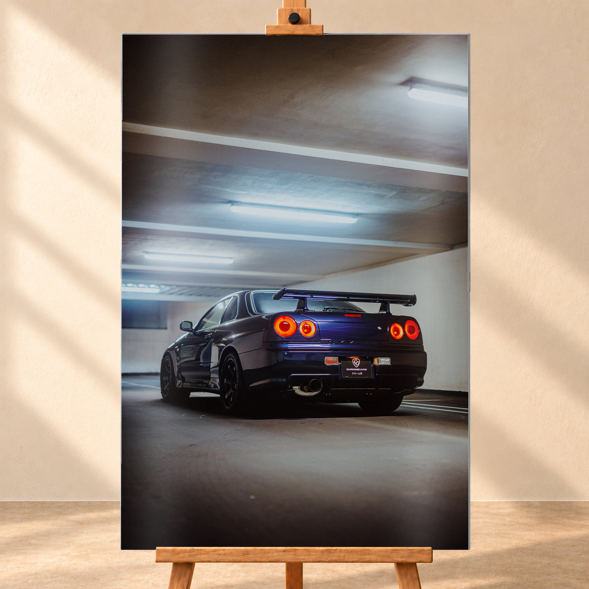 Dunkler Nissan Skyline R34 in niedriger Heck-Dreiviertelansicht mit vier rot leuchtenden Rundrückleuchten, großem Heckflügel und sichtbarem Auspuff in einer Beton-Parkgarage unter kühlen Deckenleuchten; Visualisierung als Alu gebürstet-Wandbild, frontal auf einer Holzstaffelei.