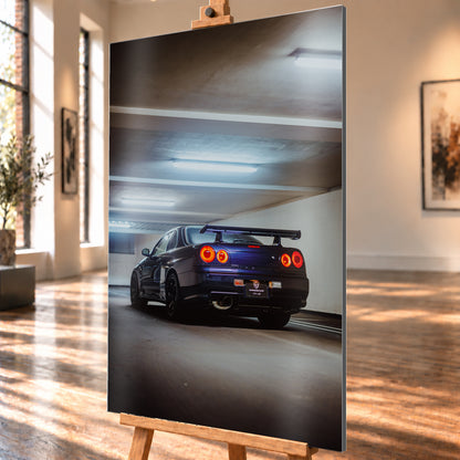 Dunkler Nissan Skyline R34 in niedriger Heck-Dreiviertelansicht mit vier rot leuchtenden Rundrückleuchten, großem Heckflügel und sichtbarem Auspuff in einer Beton-Parkgarage unter kühlen Deckenleuchten; Visualisierung als Alu gebürstet-Wandbild, schräg von der Seite auf einer Holzstaffelei.