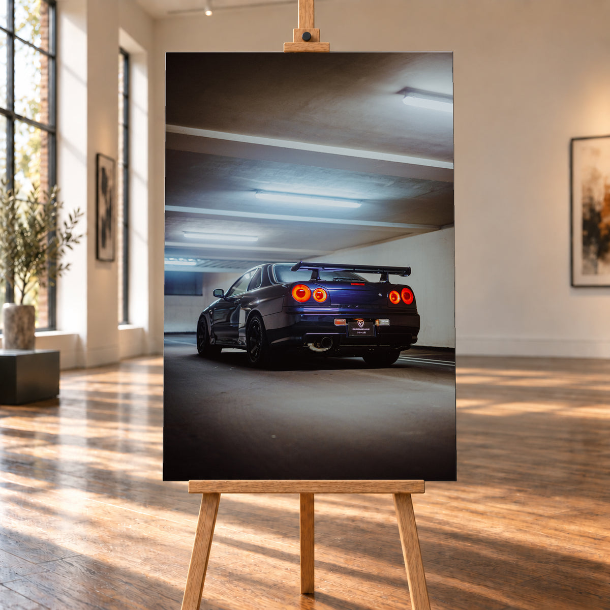 Dunkler Nissan Skyline R34 in niedriger Heck-Dreiviertelansicht mit vier rot leuchtenden Rundrückleuchten, großem Heckflügel und sichtbarem Auspuff in einer Beton-Parkgarage unter kühlen Deckenleuchten; Visualisierung als Leinwand-Wandbild, auf einer Holzstaffelei in einem hellen Galerieraum.