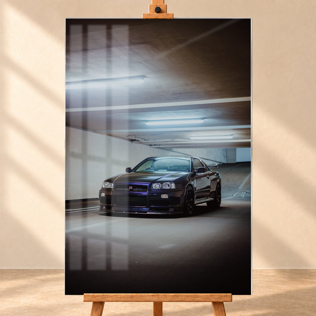 Dunkel lackierter Nissan Skyline R34 in frontaler Dreiviertelansicht in einer Betongarage mit weißen Deckenleuchten, Fahrbahnmarkierungen und ansteigender Rampe im Hintergrund; Visualisierung als Acrylglas-Wandbild, frontal auf einer Holzstaffelei.