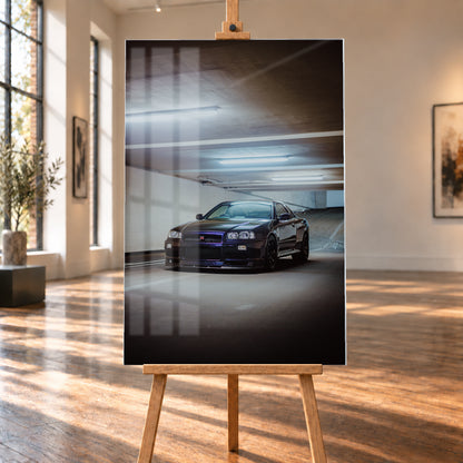 Dunkel lackierter Nissan Skyline R34 in frontaler Dreiviertelansicht in einer Betongarage mit weißen Deckenleuchten, Fahrbahnmarkierungen und ansteigender Rampe im Hintergrund; Visualisierung als Acrylglas-Wandbild, auf einer Holzstaffelei in einem hellen Galerieraum.