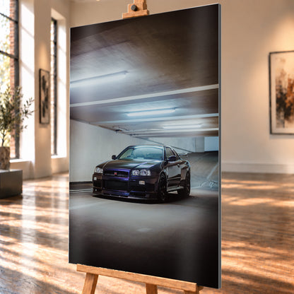 Dunkel lackierter Nissan Skyline R34 in frontaler Dreiviertelansicht in einer Betongarage mit weißen Deckenleuchten, Fahrbahnmarkierungen und ansteigender Rampe im Hintergrund; Visualisierung als Alu gebürstet-Wandbild, schräg von der Seite auf einer Holzstaffelei.